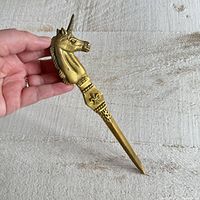 Front angle view of the vintage solid brass letter opener showing the unicorn head handle and fleur-de-lis decoration on the shaft.