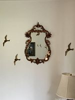 Front view of the vintage Syroco mirror mounted on the wall surrounded by brass bird wall decorations.