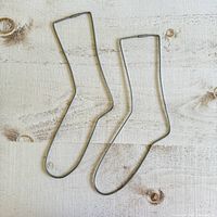 Top view photo of two vintage wire frame sock stretchers laid flat on light wood surface, showing sock outline shape and metal construction.