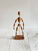 Front view of the full wooden artist drawing mannequin on wooden base against a light background.