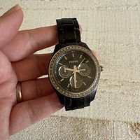 Front view of the black Fossil women's watch held in hand showing the face with three subdials and crystal bezel.