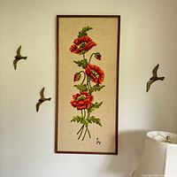 Full view of the large crewel embroidery artwork with three prominent red poppies framed on wall.