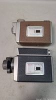 Two vintage 8mm movie cameras, one Brownie Cine Scopemeter in black texturing and one Kodak with brown textured exterior, placed side by side.