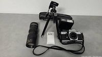 Lot items arranged on table showing camera body, lens, flash, tripod, and tag with lot number 822