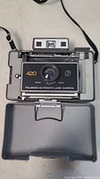 Top-down view of the Polaroid 420 Automatic Land Camera inside original box with strap, showing front lens and exposure settings.