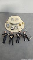Four Beatles toy figures with instruments and accessories laid out with a round white stand.