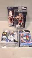 Lot of three toy sports figures in original packages showing front view, includes UFC Georges St-Pierre, Andrew Luck Colts player, and Colin Kaepernick 49ers player figures.