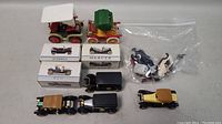 Lot showing several vintage toy cars including three in original branded boxes (Hupmobile, REO, Mercer) along with other cars and toy parts in a clear bag.