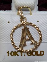 10K gold pendant with letter 'A' inside twisted circular frame on a display tray marked '10KT. GOLD'