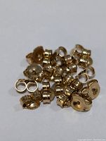Close-up image showing approximately 27 small 10K gold earring backs with a polished metallic yellow finish.