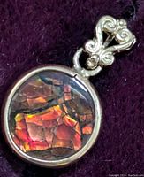 Close-up photo of the front of the round ammolite pendant showing the vibrant fractured iridescent gem with a gold bezel and ornate bail.