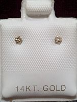 Front view of the pair of 14K gold diamond stud earrings displayed on a white textured holder labeled '14KT. GOLD'.