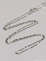 Full view of a thin, faceted 18K gold chain necklace laid out on white background, showing the length and delicate links.