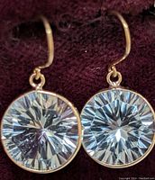 Pair of yellow gold drop earrings with round faceted blue topaz stones against burgundy background