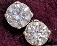 Close-up of two round brilliant diamonds in four-prong 14K gold stud settings on dark purple background