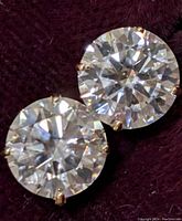 Two round moissanite stud earrings on burgundy cloth showing front view.