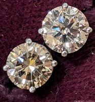 Close-up view of both round brilliant-cut stones in four-prong settings on burgundy background