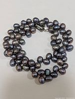Top view of dark freshwater pearl necklace arranged in a loop, showing the iridescent quality of the pearls and the stainless steel clasp.