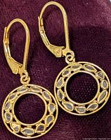 Close-up photo of gold-tone stainless steel drop earrings with open circle design and embedded natural rough diamond chips on soft fabric background.