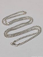 Full view of the silver chain necklace laid out in a serpentine shape showing clasp and links.