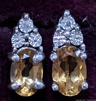 Close-up front view of the pair of sterling silver citrine and diamond earrings on a dark background.