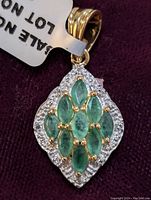 Close-up of the pendant showing emeralds, diamond halo, and gold-tone bail.