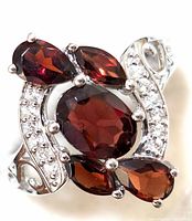 Close-up of sterling silver ring featuring central oval garnet surrounded by smaller garnet stones and cubic zirconia accents in a swirling design.