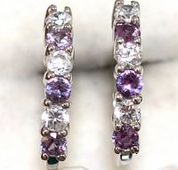 Close-up front view showing the alternating purple and clear round faceted gemstones set in sterling silver hoops.