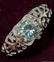 Close-up image showing front view of sterling silver ring with round moissanite center gemstone on a dark background.