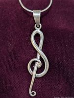 Close-up front view of sterling silver treble clef pendant on snake chain necklace against maroon fabric background