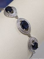 Close-up of bracelet showing blue sapphire stones and surrounding small cubic zirconia stones on a sterling silver setting.