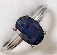 Close-up view of oval faceted blue sapphire in four-prong sterling silver setting