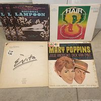 Four vinyl LP records laid out showing front album covers, including National Lampoon, Hair, Mary Poppins, and one with a signed white cover.