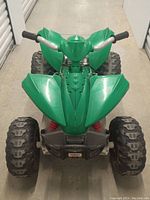 Front view of green All Terrain Tex Power Wheels ATV showing large knobby tires, green plastic body and handlebar grips.