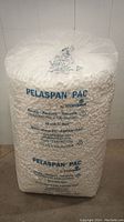 Front view of the 20 cubic feet sealed plastic bag of white Pelaspan PAC packing peanuts, showing branding and text.