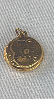 Photo of round gold pendant from the front showing detailed floral and scroll engraving
