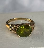 Close up of the gold ring with a green faceted oval stone showing the stone color and cut details along with the ring setting.