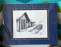 Black and white drawing of a train depot with a steam locomotive, set on railroad tracks, matted in blue with black and white borders.