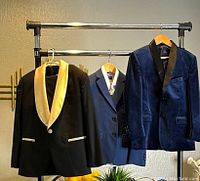 Three formal boys jackets (black with gold collar, blue velvet with black collar, and blue suit jacket) displayed on a clothing rack