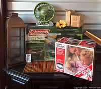 Full lot photo showing Coleman box, vaporizer box, small green fan, metal lantern, and two boxes of LED lights on dark surface.