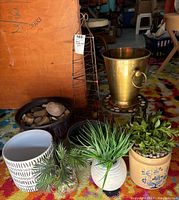 Wide angle photo showing all items in the lot including brass planter, rustic tower, mosaic stone stand, faux plants and pots