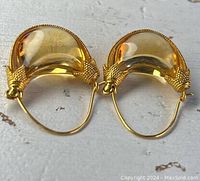 Top view of pair of gold earrings with translucent gold crescent stones and detailed gold setting.