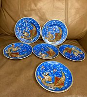 Six vintage Japanese Morige dragon design plates arranged on leather surface showing vibrant blue background with raised colorful dragon motif.