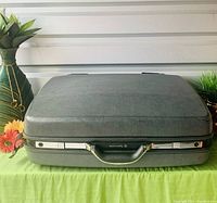 Closed grey Samsonite hardbody suitcase on wheels laid flat with handle side facing front. Shows textured case surface and chrome trim above the handle.