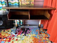 Full side view of vintage Drexel Et Cetera bar server showing black laminate top, open shelving divided into two compartments, and gilded cast iron base with turned legs.