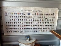 Full view of the NASA Human Space Flight Awareness poster showing rows of mission patches from 1963 to 2003, with visible aging and a small rip near the center-right.