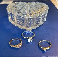 Photo showing the heart-shaped glass trinket box and three rings arranged on a blue surface.