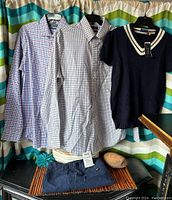 Two Ralph Lauren plaid shirts, one medium regular fit and one stretch fit, hung alongside a vintage-style blue short sleeve sweater with white V-neck stripes above a pair of navy blue Ralph Lauren 100% cotton shorts.
