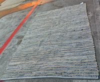 Full view of the rectangular handwoven rug laid out on concrete surface, showing woven denim and jute texture and color pattern.