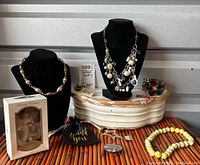 Full lot of signed jewelry displayed on stands and surface including necklaces, bracelet, pins, ring, and boxed ornament.